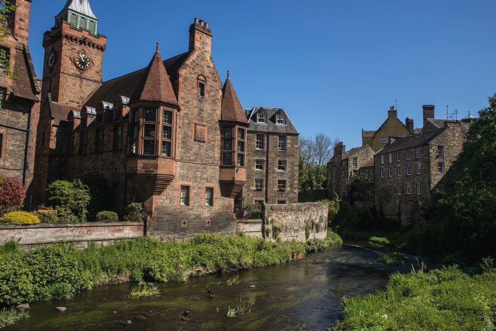 A clock tower and other brown buildings alongside a river under a clear sky