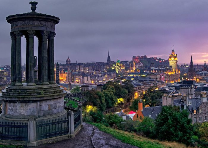 A stone monument on a hill, and city skyline.