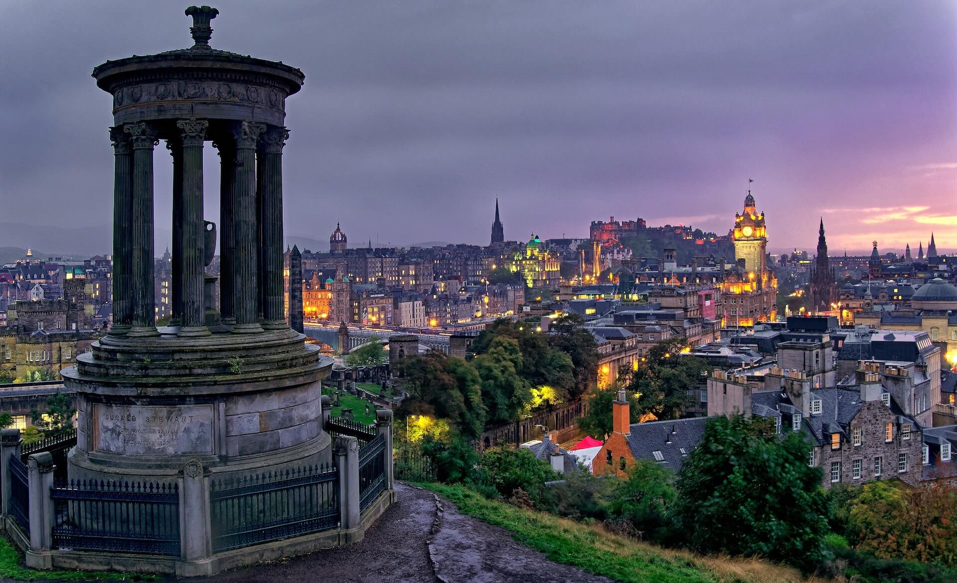 A stone monument on a hill, and city skyline.